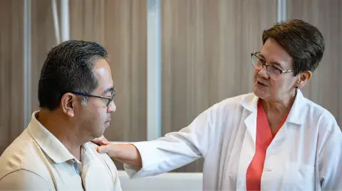 A doctor in a white coat places her hand on the shoulder of a Veteran patient.